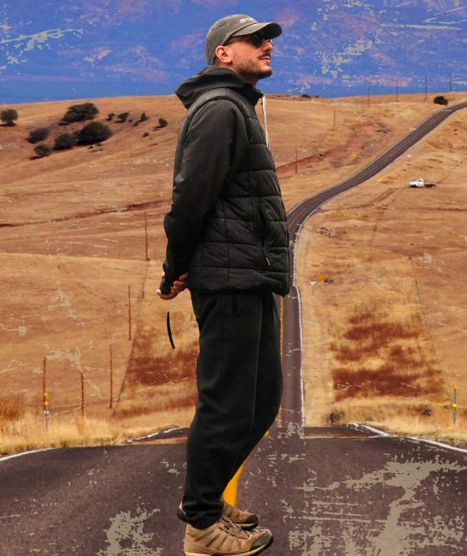 Lucas parado en el medio de una ruta, con montañas al fondo